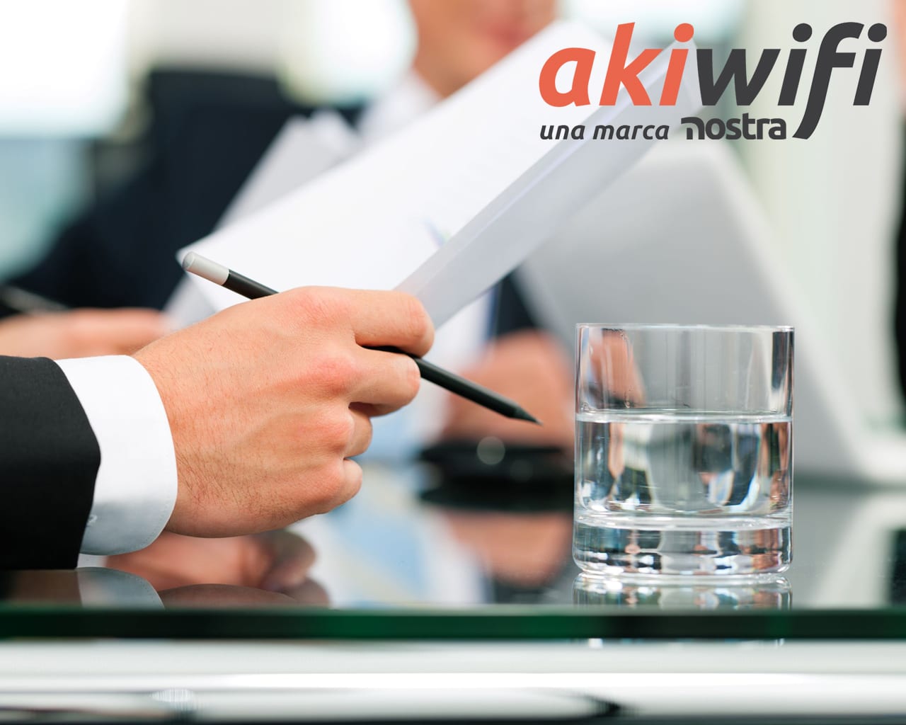 Primer plano de una mano firmando un documento junto a un vaso de agua, con el logo de akiwifi