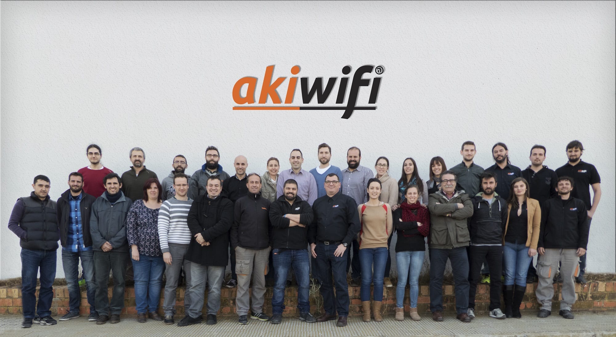 Equipo de Akiwifi posando en grupo frente a una pared blanca con el logo de la marca