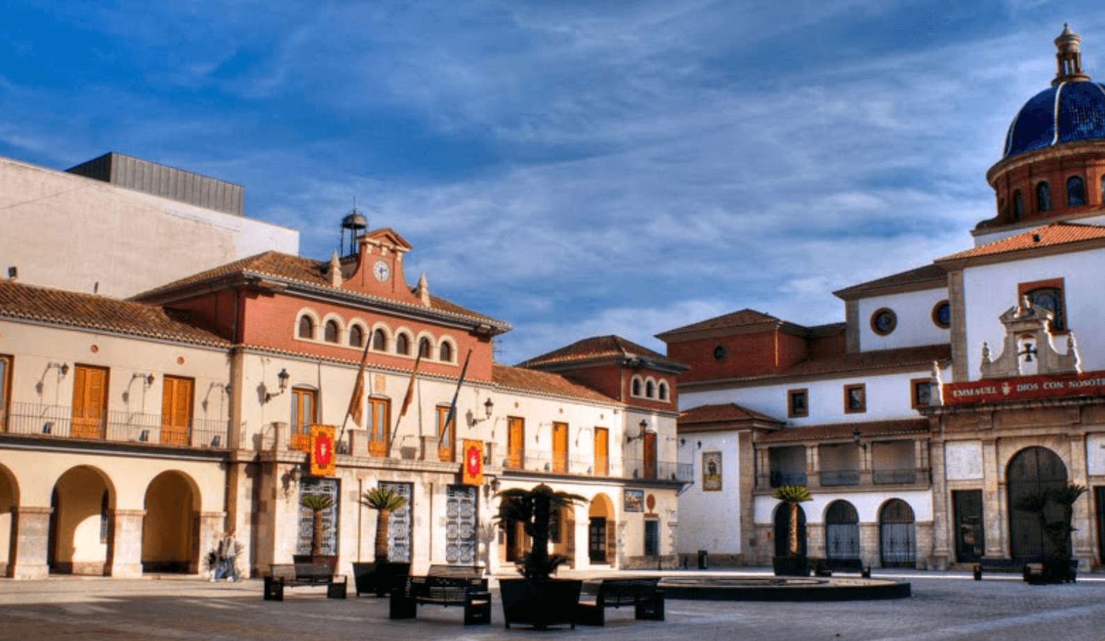 Plaza mayor de un municipio con el ayuntamiento y una cúpula al fondo