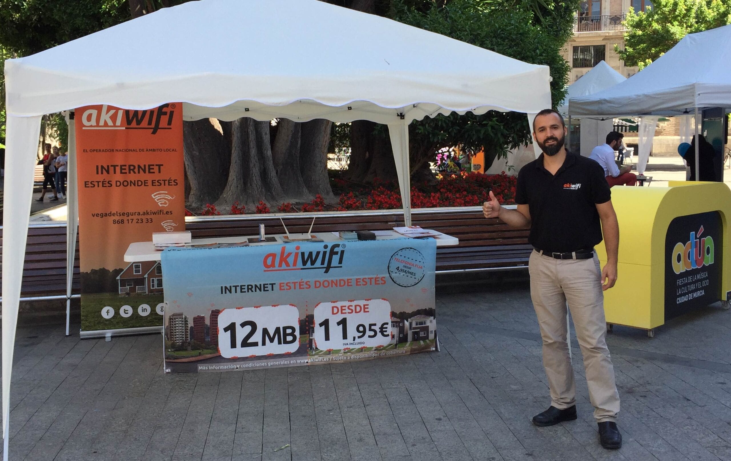 Técnico de akiwifi con el pulgar levantado junto al estand de la marca en la fiesta Actúa de Murcia