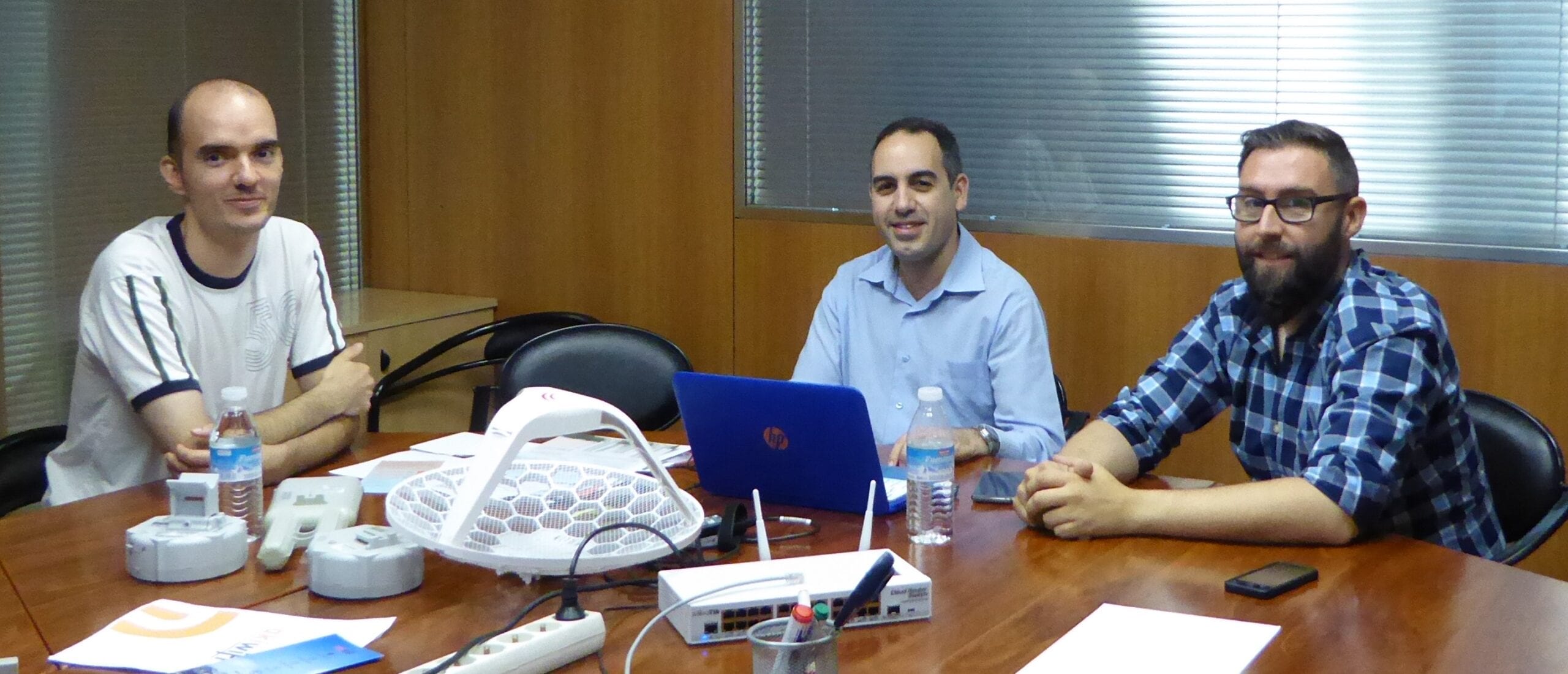 Tres técnicos de akiwifi en una sala de reuniones con antenas y routers sobre la mesa