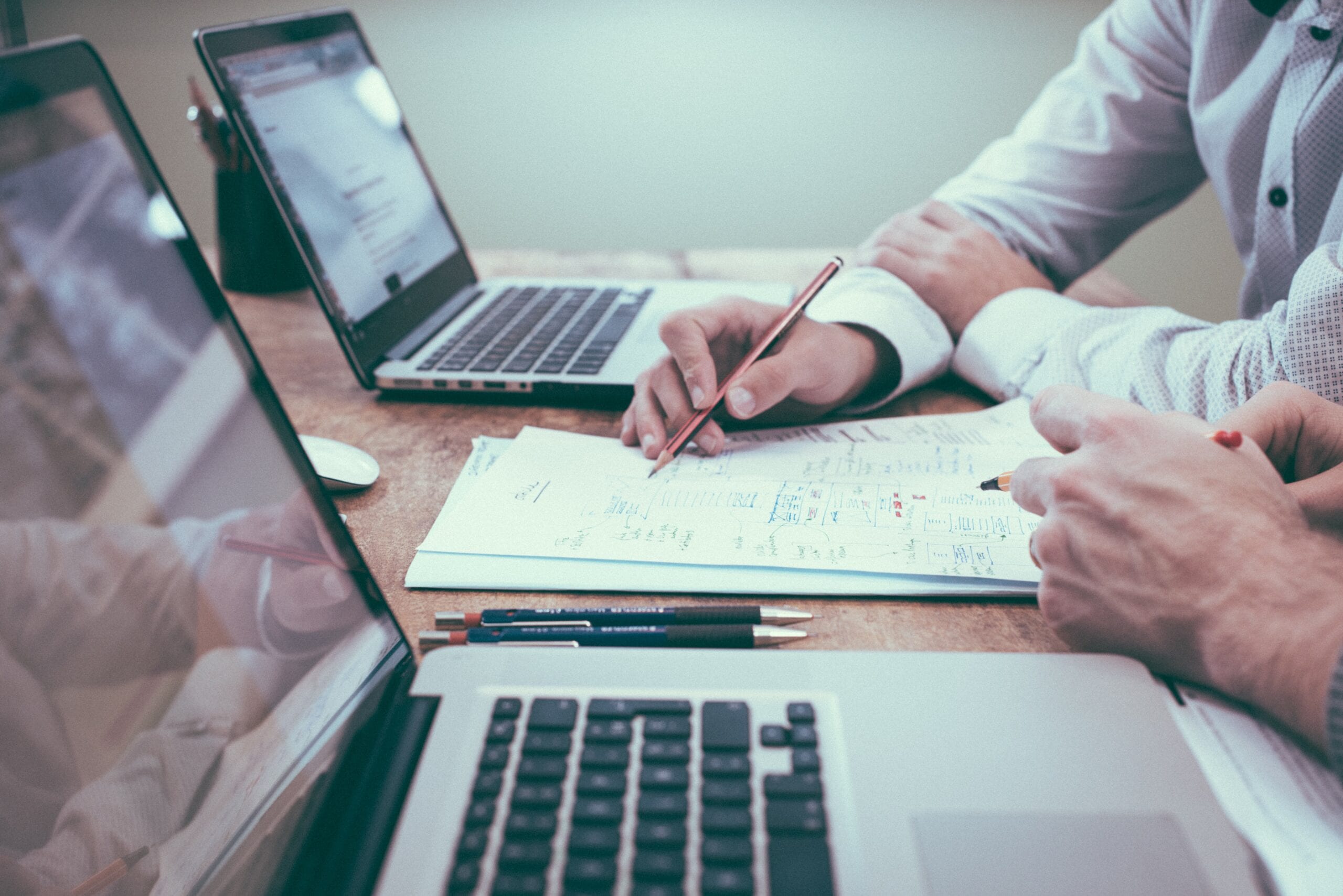 Dos profesionales trabajando con portátiles y documentos con gráficos sobre una mesa