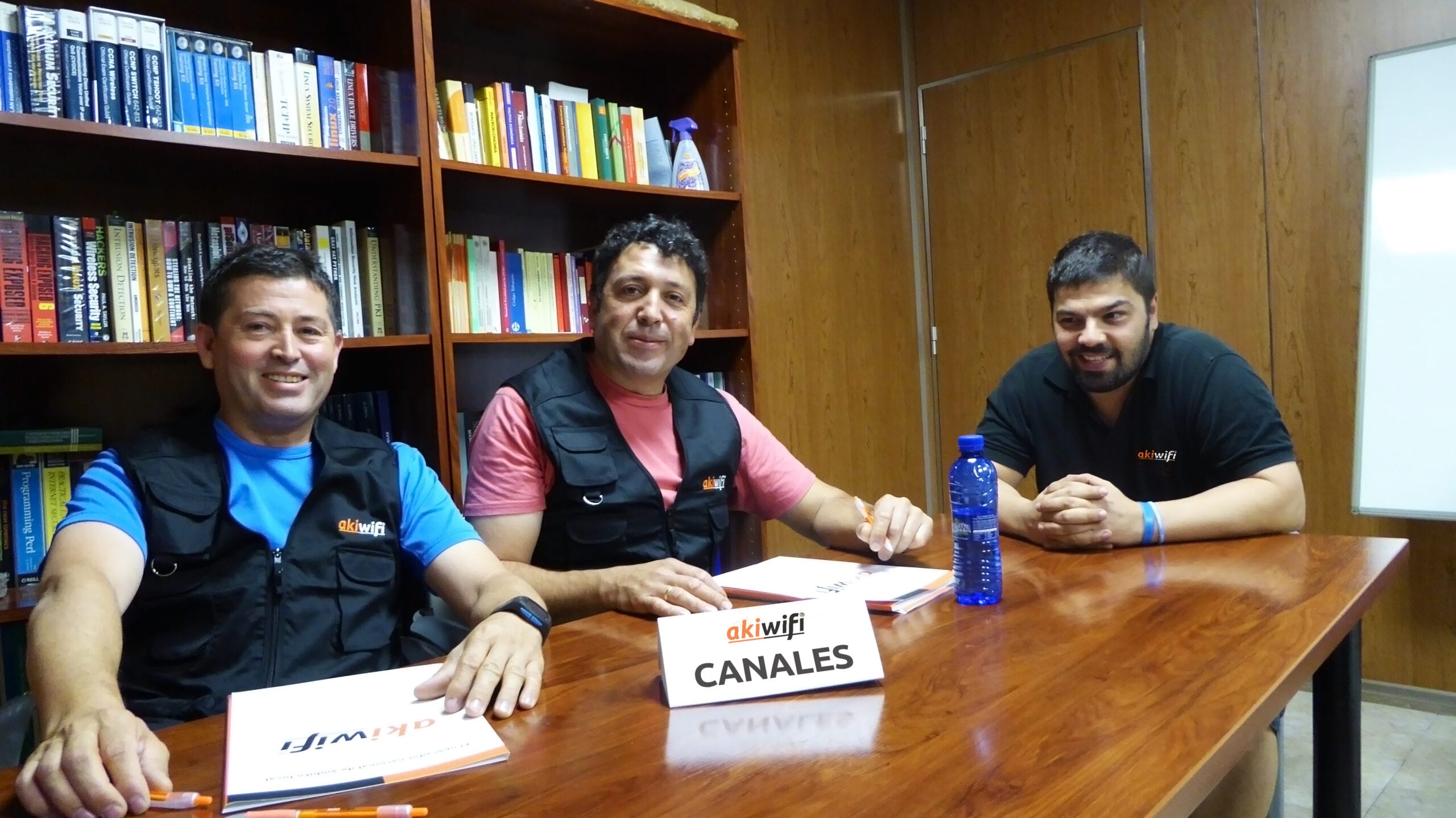 Tres técnicos de akiwifi reunidos en un despacho, con el cartel «Canales» sobre la mesa
