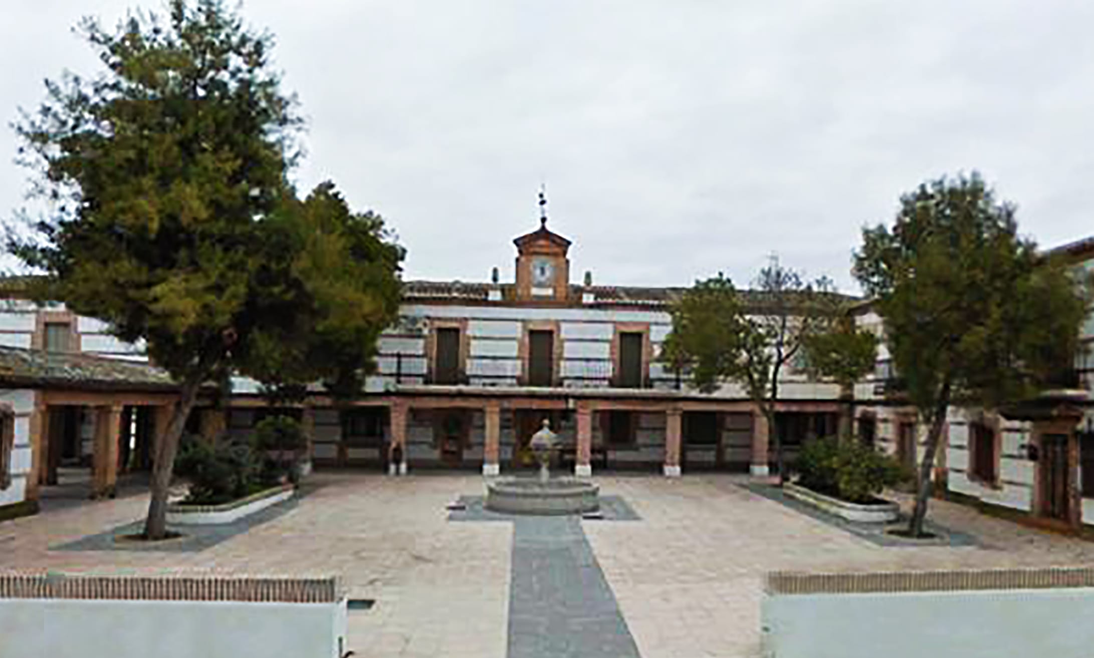 Patio interior de un edificio histórico con torre y reloj, columnas y jardín