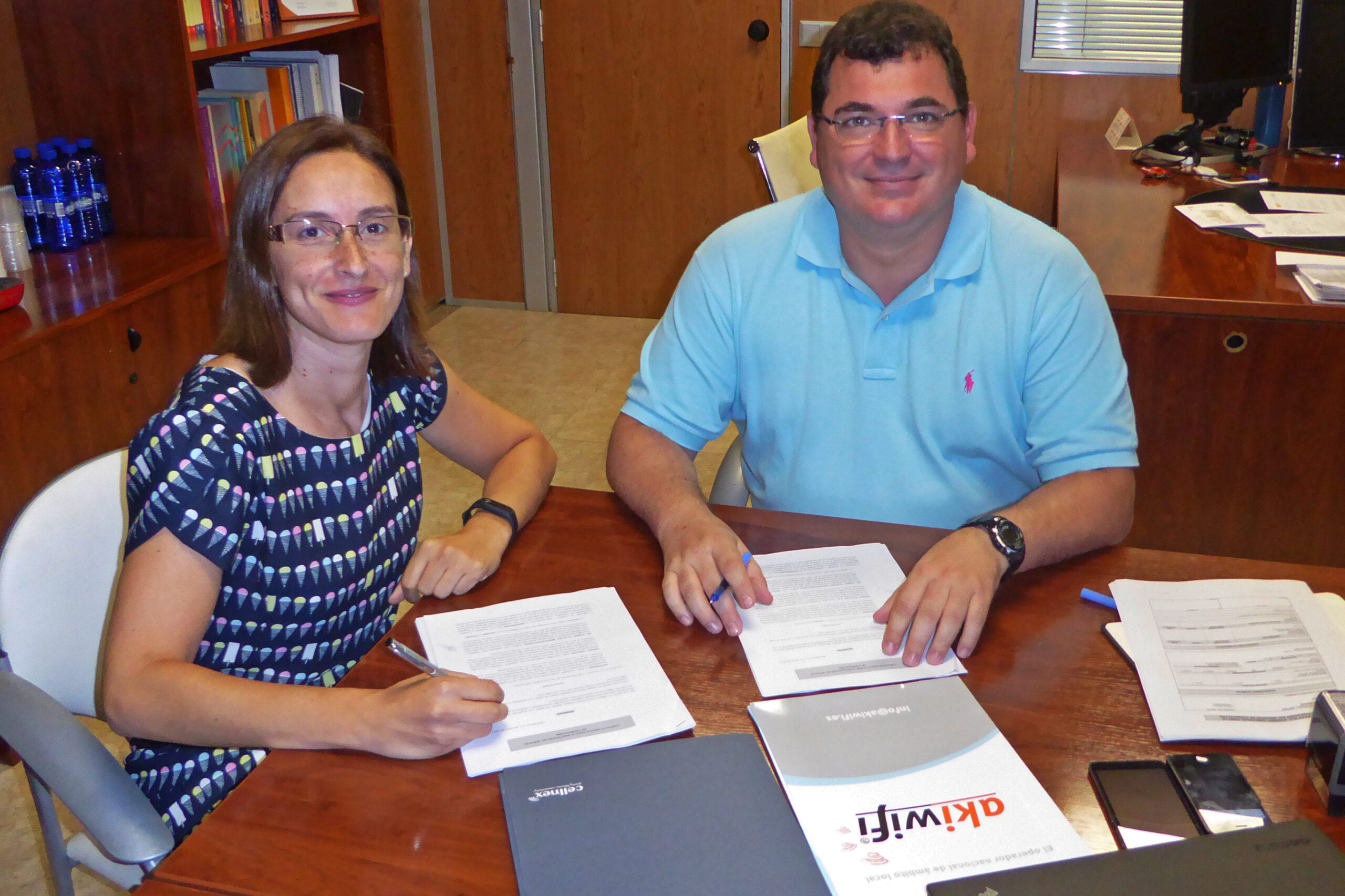 Dos personas firmando un acuerdo en una oficina, con carpetas de akiwifi y Cellnex sobre la mesa