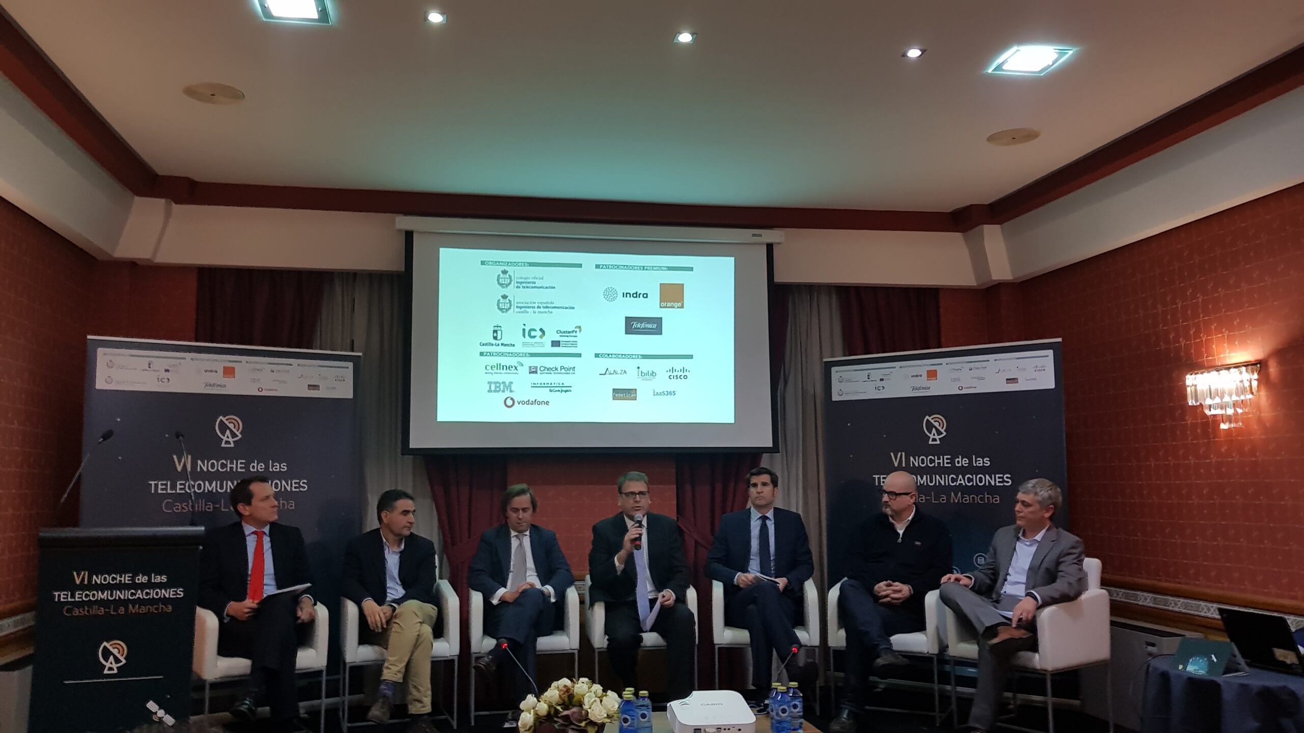 Mesa redonda de ponentes durante la Noche de las Telecomunicaciones de Castilla-La Mancha, con los patrocinadores proyectados en pantalla