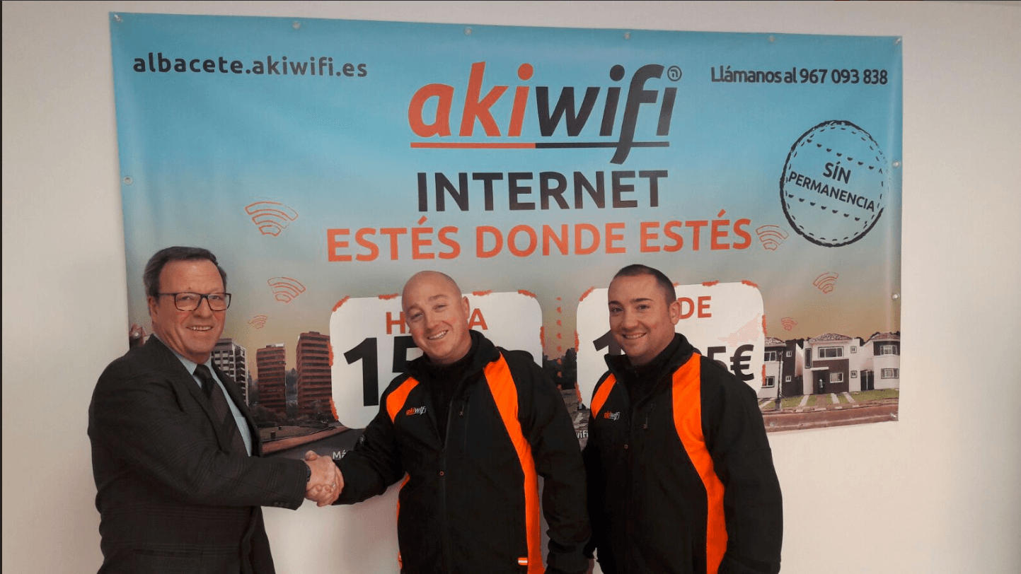 Dos técnicos de akiwifi con el director estrechándose la mano ante un banner publicitario de akiwifi Albacete