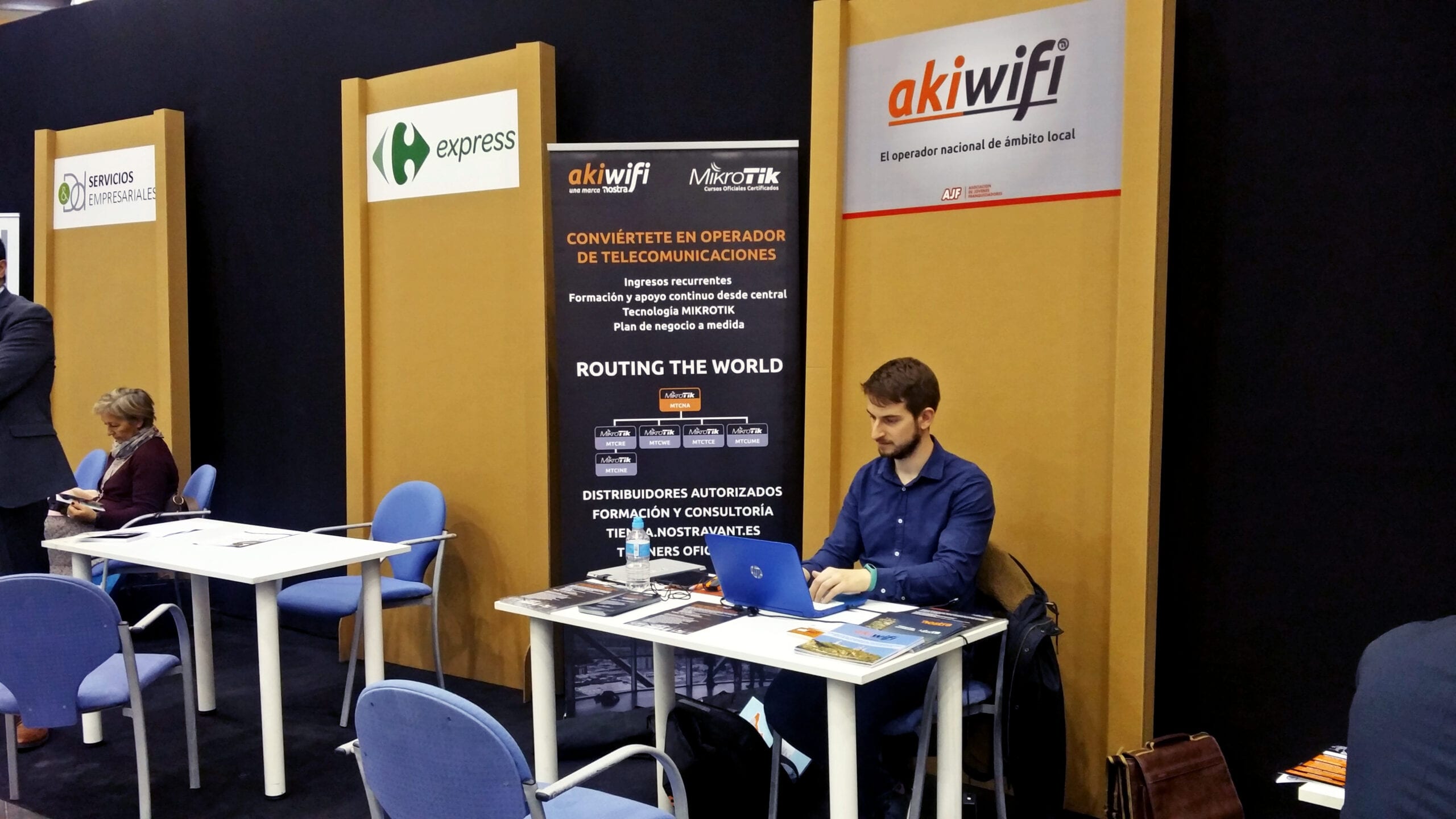 Estand de akiwifi en una feria de franquicias, con un comercial trabajando en su portátil junto a los paneles informativos de la marca
