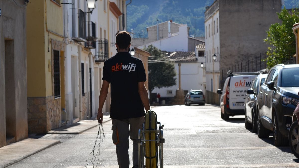 Técnico de akiwifi de espaldas caminando por una calle con una bobina de cable de fibra óptica