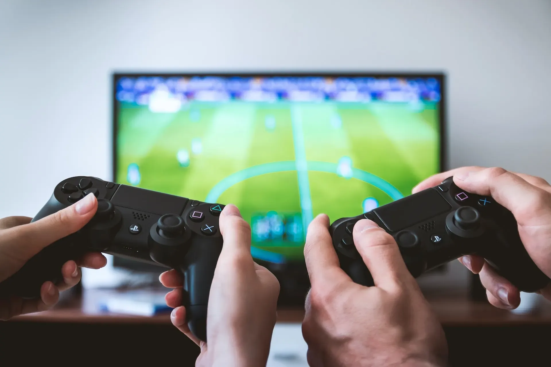 Dos personas jugando a un videojuego de fútbol con mandos de PlayStation frente al televisor