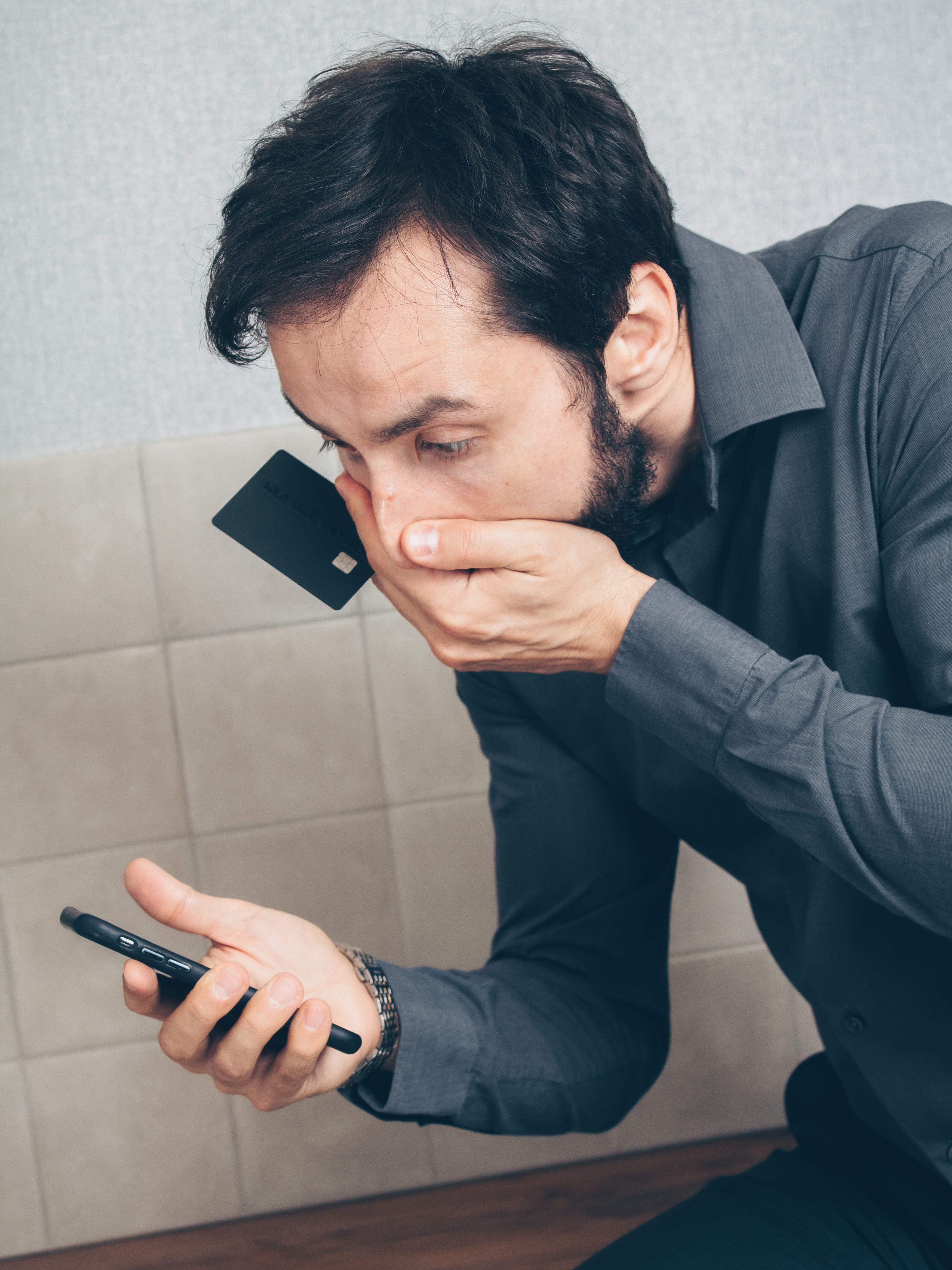 Hombre con gesto de sorpresa y preocupación mirando el móvil mientras sujeta una tarjeta de crédito